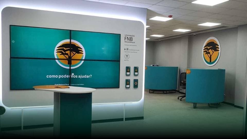 Instalação de digital signage e TV corporativa no balcão FNB Moçambique, com videowall e mensagem «como podemos ajudar?».